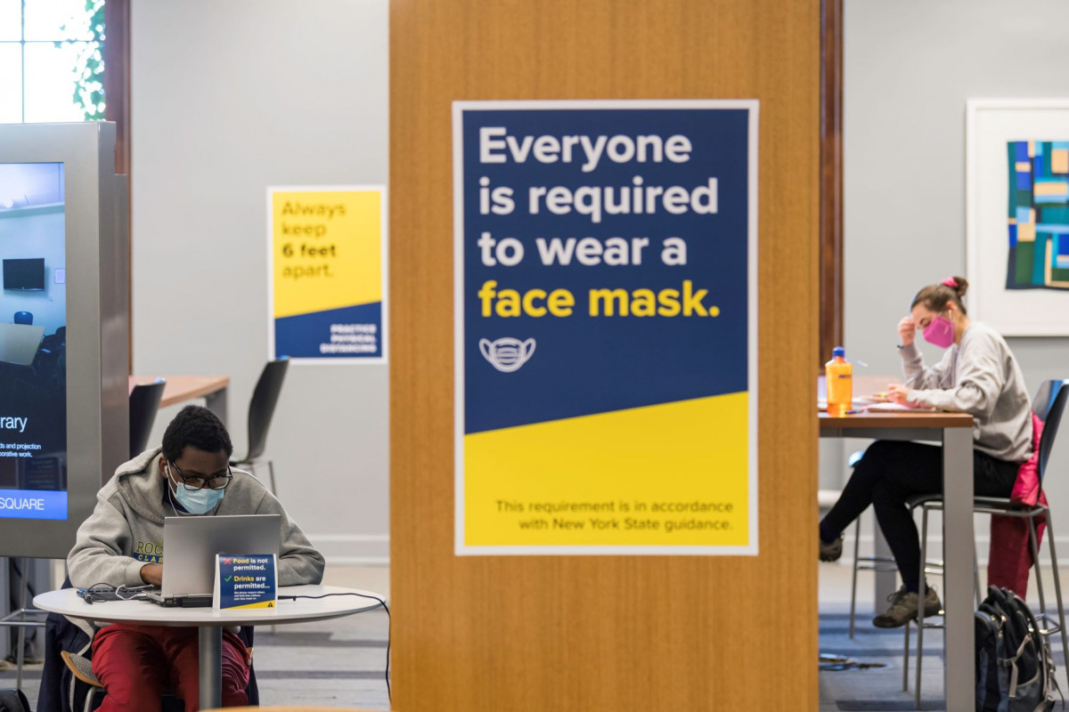 Masked students in Rush Rhees Library and a sign saying everyone must wear a face mask