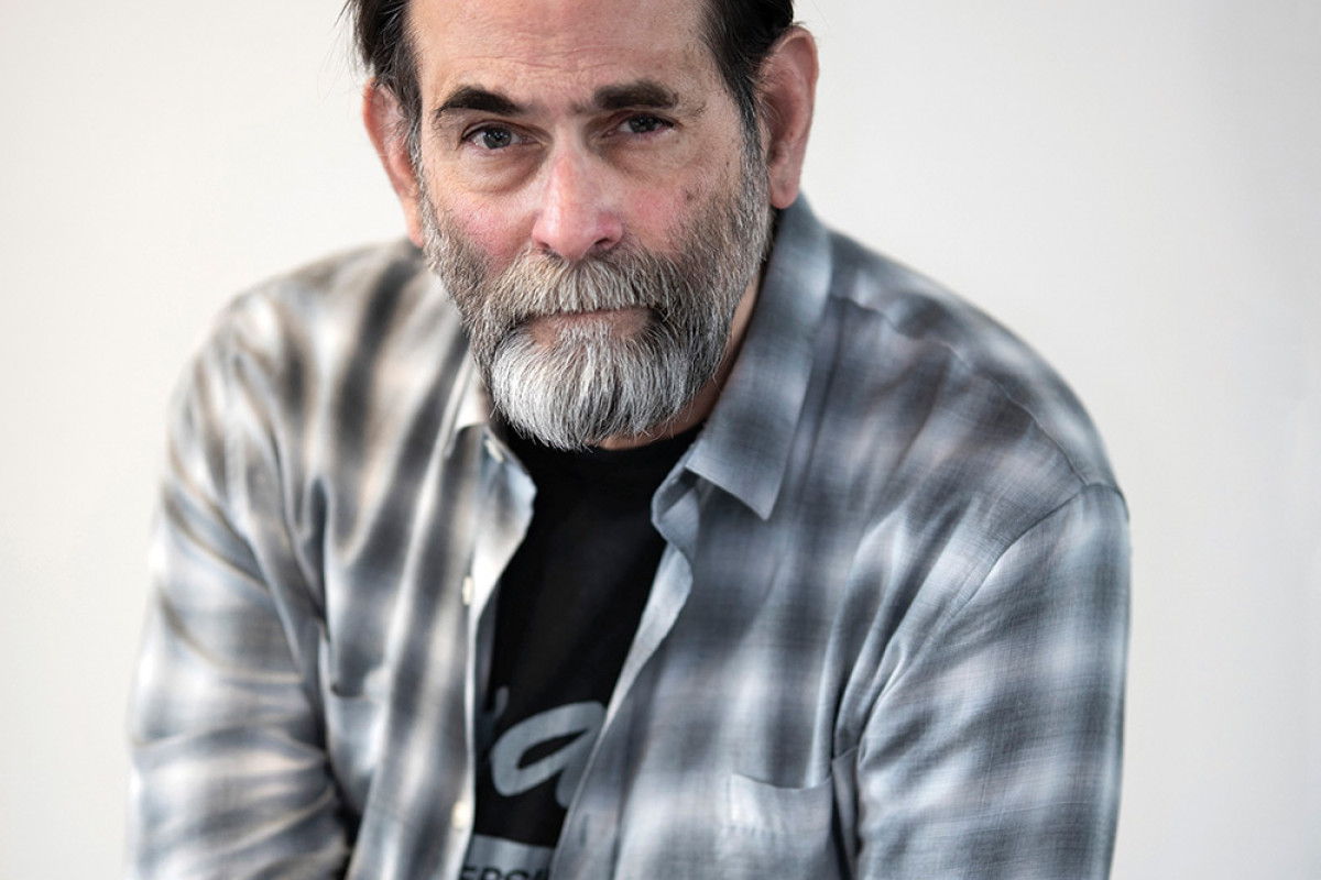 Portrait of a bearded Avram Finkelstein in a plaid shirt from the waist up