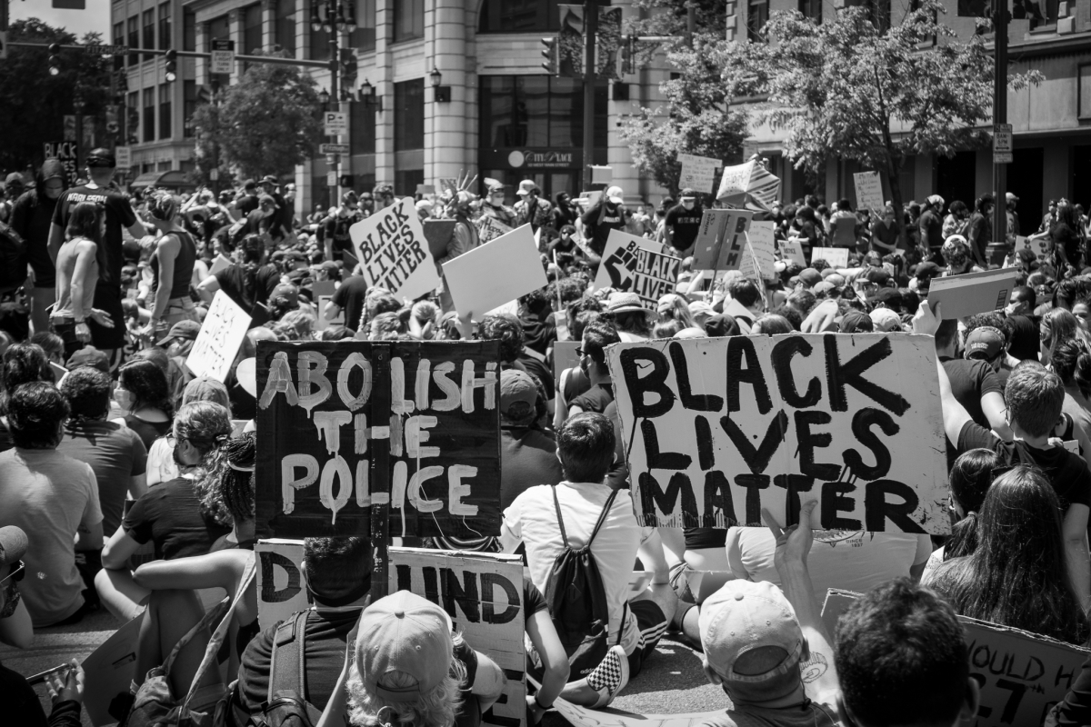Black and white photo of a protest with prominent "Black Lives Matter" and "Abolish the Police" posters
