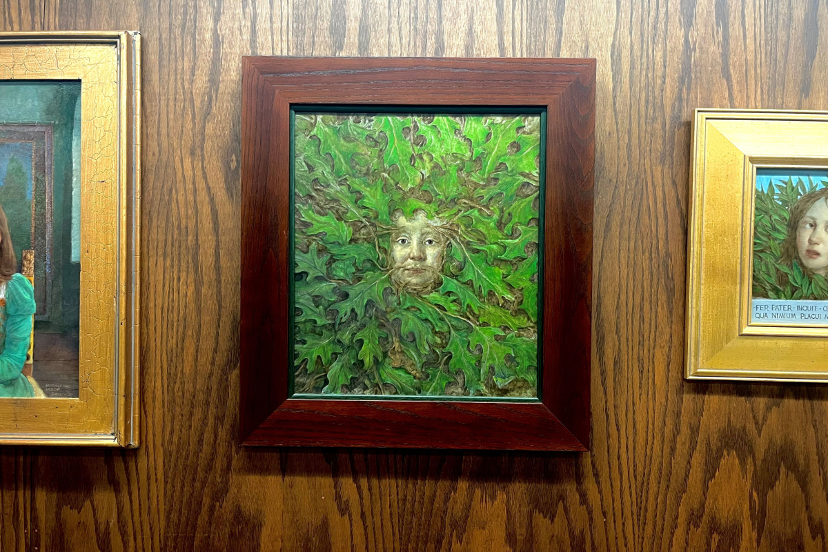 A framed painting, at center a face with green leaves growing out of it