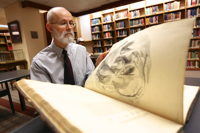Christopher Hoolihan in Miner Library holding open a very large, old book
