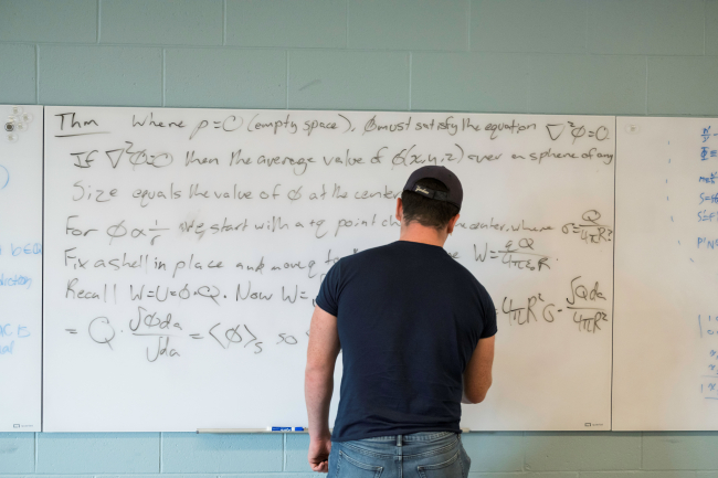 A student writing on a whiteboard filled with equations