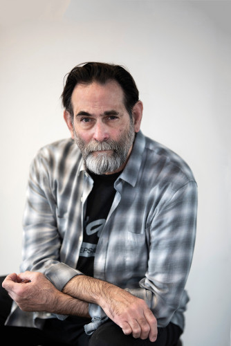 Portrait of a bearded Avram Finkelstein in a plaid shirt from the waist up
