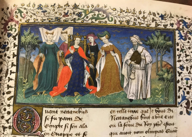 Queen Olympias sits on a throne in a field. She is surrounded by four noblewomen and a man. They are all dressed in beautiful clothing. 