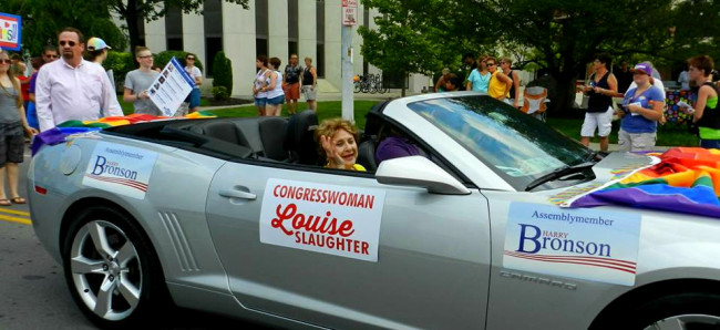 Louise Slaughter riding in a silver Camaro decorated with rainbow bunting