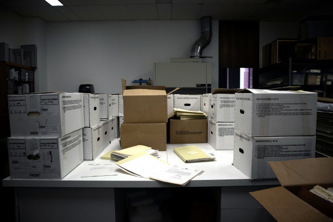 A table covered in banker's boxes, folders, and papers