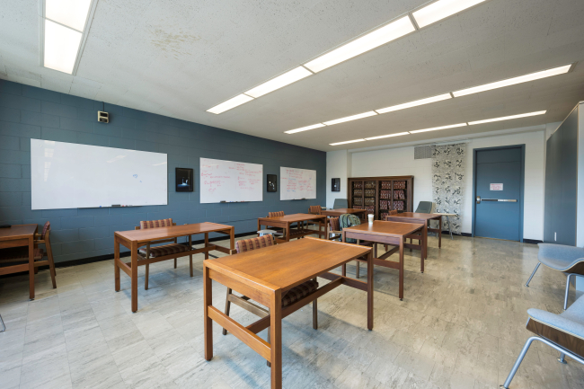 A view of POA's quiet room, showing four tables, three whiteboards, a book case, and exit door