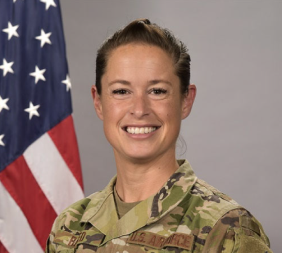 Lieutenant Cololnel Stephanie Raffo wearing military fatigues standing in front of a flag.
