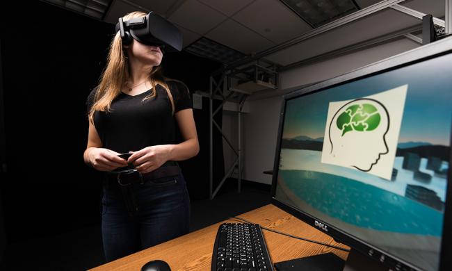 Brenna James '20 wearing a virtual reality headset with a computer in the foreground of the photo	