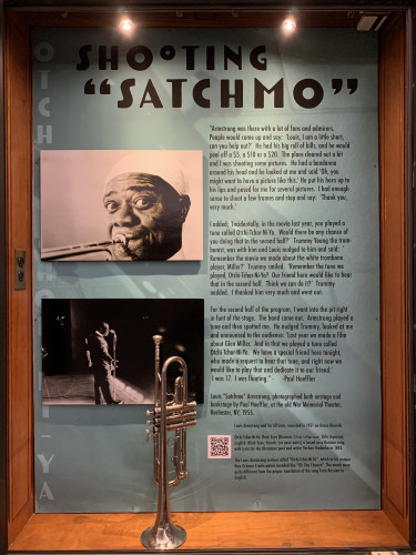 "Shooting 'Satchmo'" jazz exhibit case with 2 photographs, text, and a silver trumpet