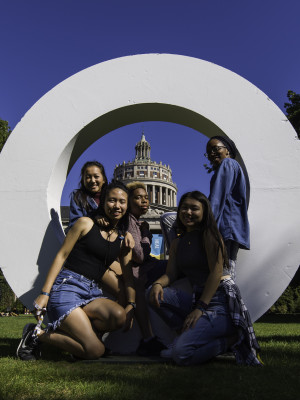 Photo of students sitting in front of the O in Meliora on the quad lawn